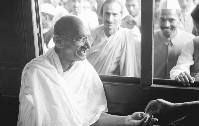 Fotografia em preto e branco de Mahatma Gandhi dentro de um veículo recebendo fãs e seguidores pela janela.