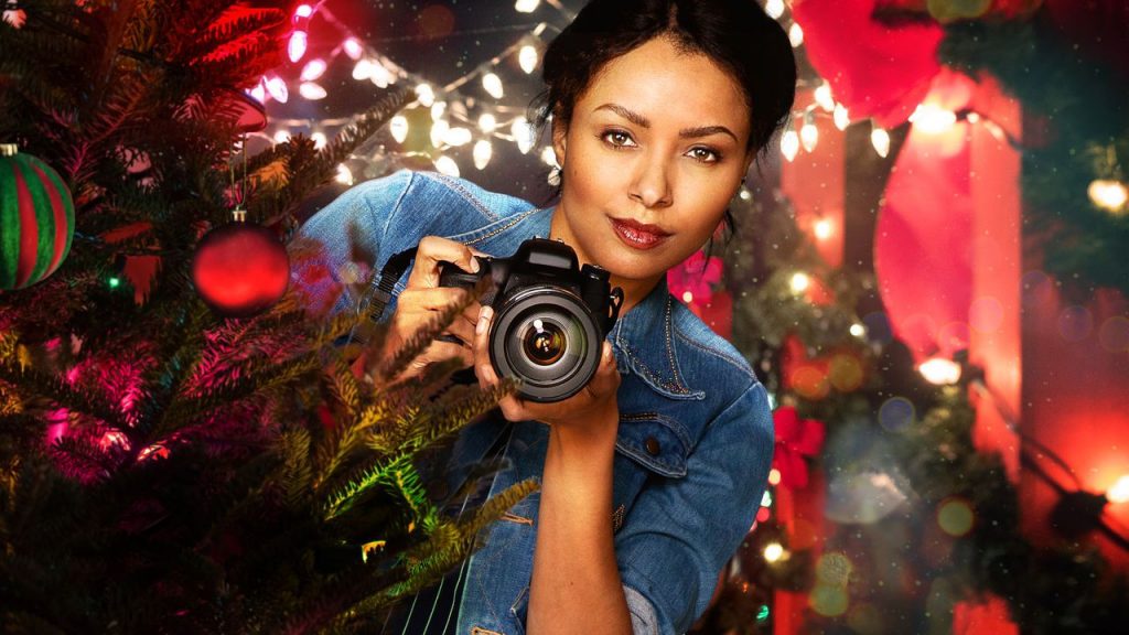 Pôster do filme "O Feitiço do Natal", em que a protagonista segura uma câmera em meio a decorações de Natal.