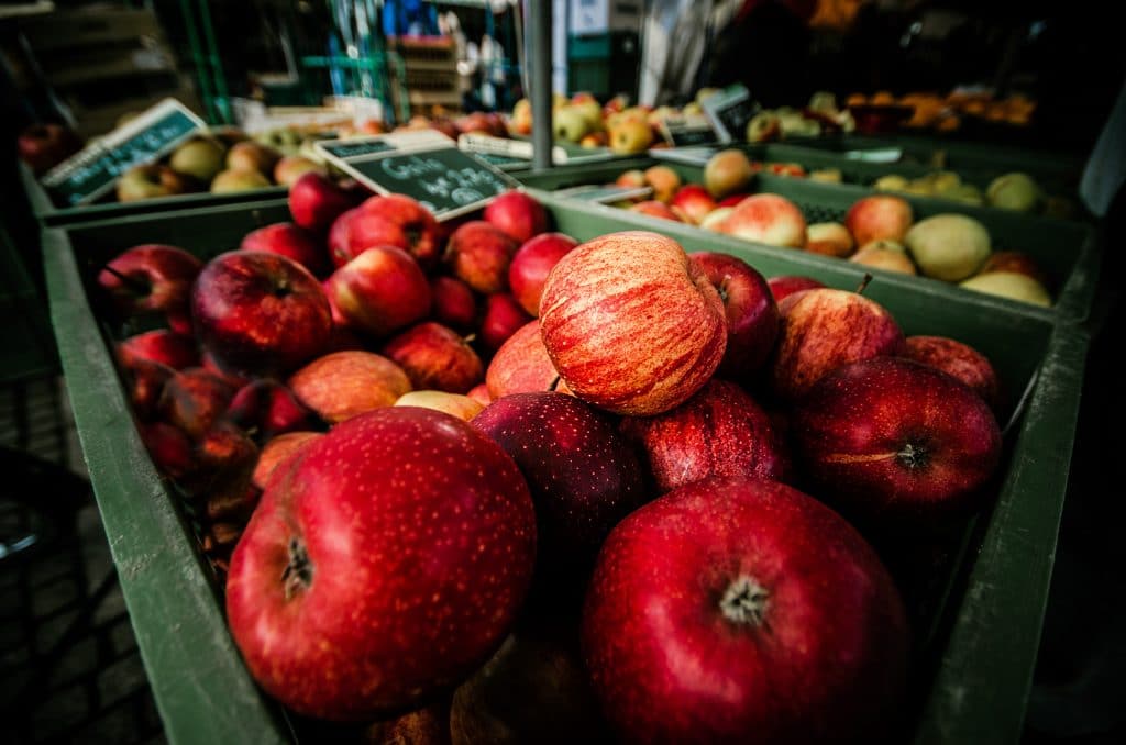 Maças vermelhas em caixa de mercado com frutas ao fundo