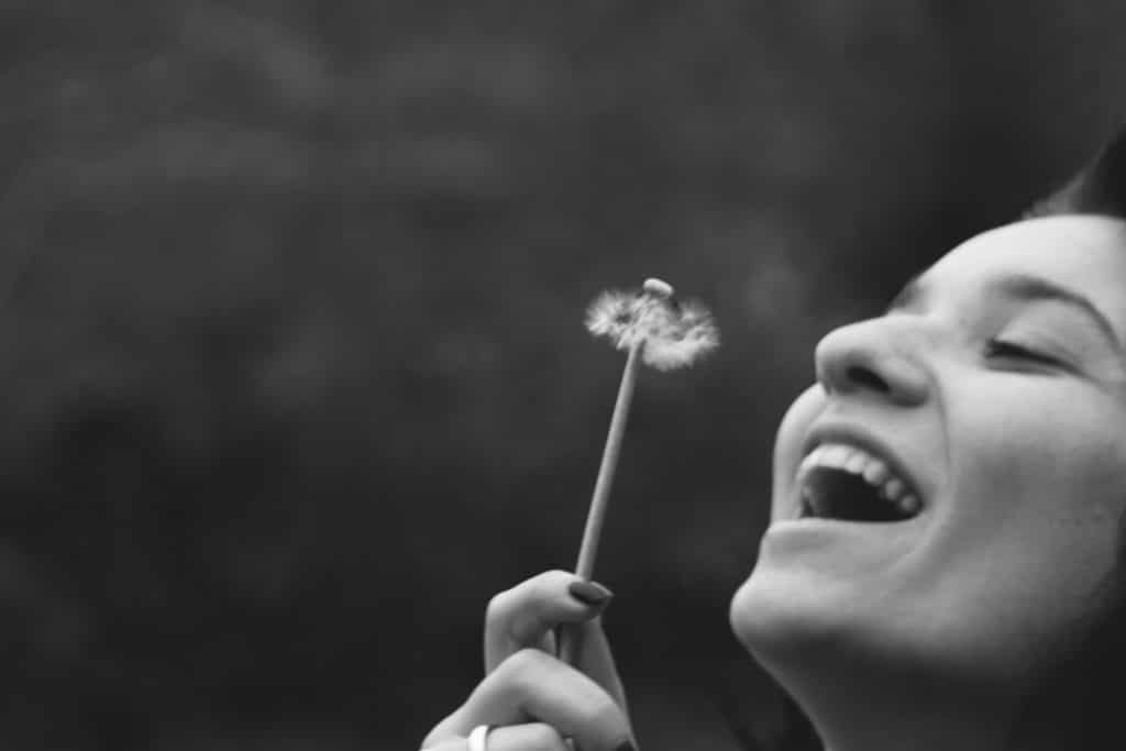 Mulher sorrindo segurando flor dente-de-leão em preto e branco