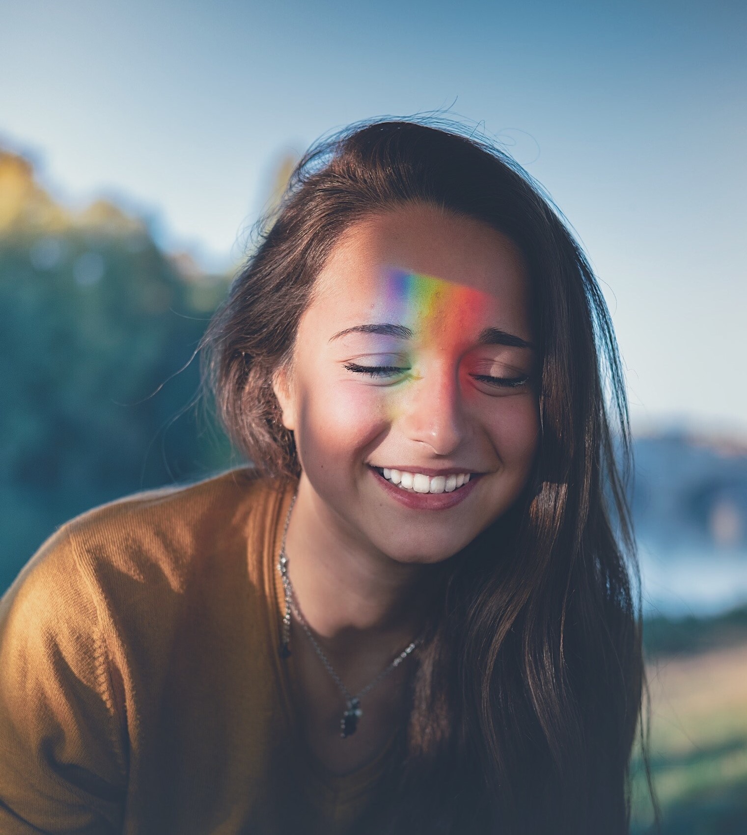 Mulher com os olhos fechado e sorrindo, com arco iris no rosto.