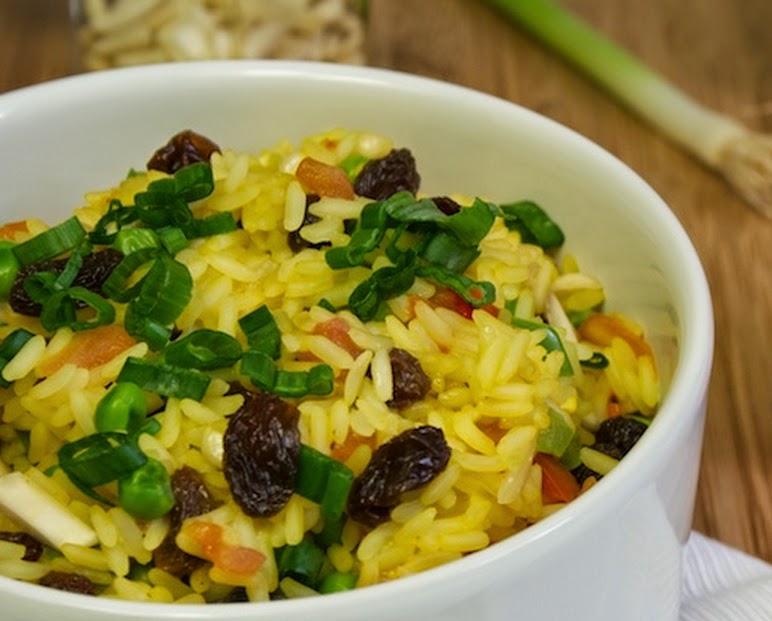 Arroz colorido em uma tigela. É possível ver cebolinha, uva passa e pimentão entre o arroz.