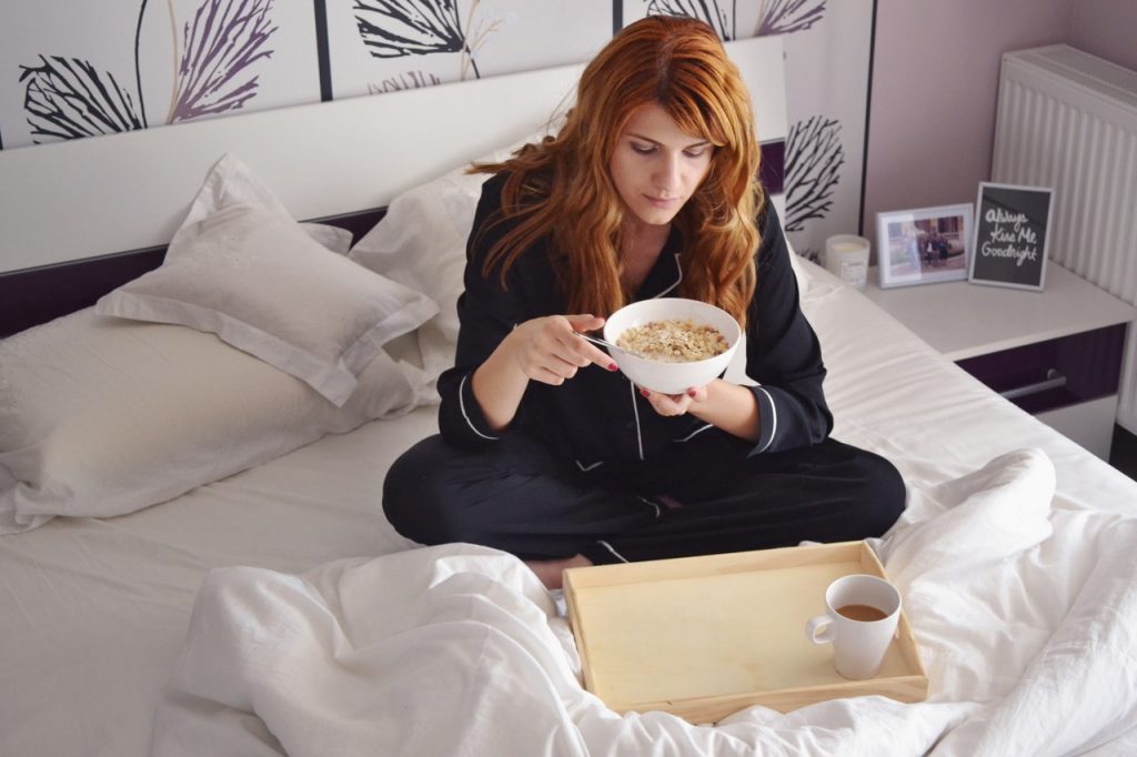 Mulher ruiva, sentada na cama, tomando café da manhã.