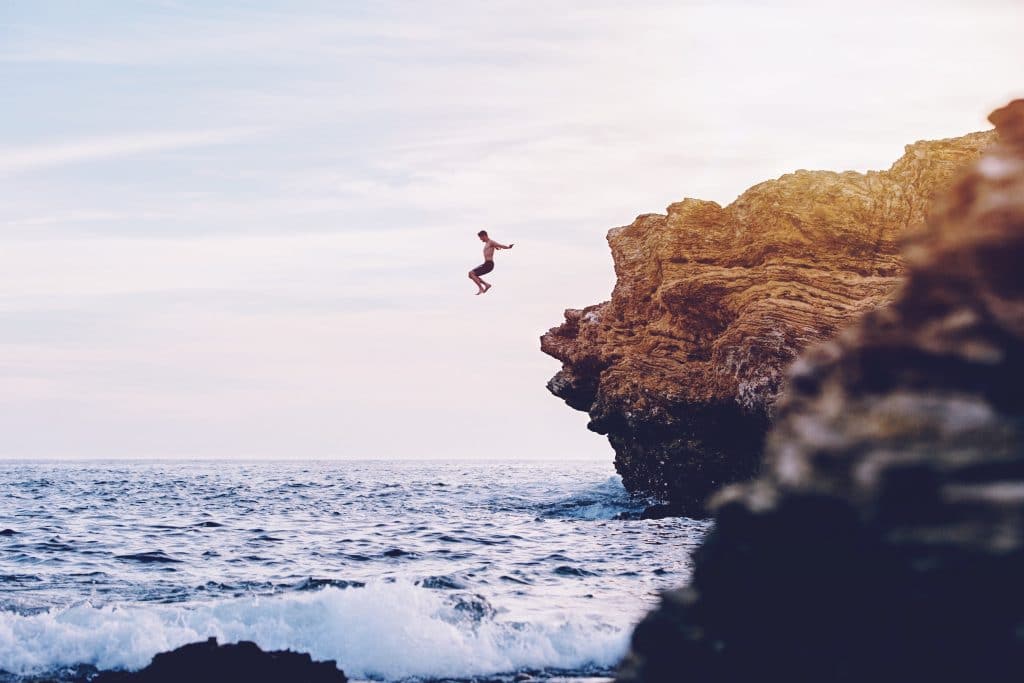 Homem pulando de pedra em mar