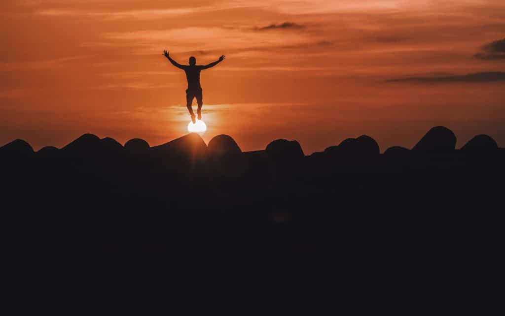 Silhueta de pessoa pulando com sol e montanhas ao fundo