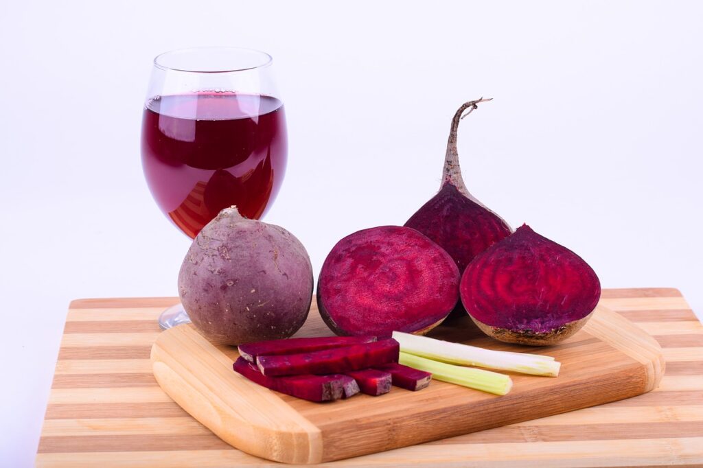 Tábua de madeira com beterrabas inteiras e fatiadas, ao lado de uma taça com suco de beterraba.