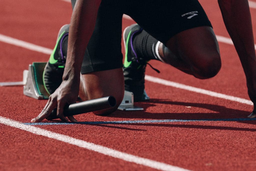 Imagem ampliada de um atleta ajoelhado, momentos antes de dar início à corrida.