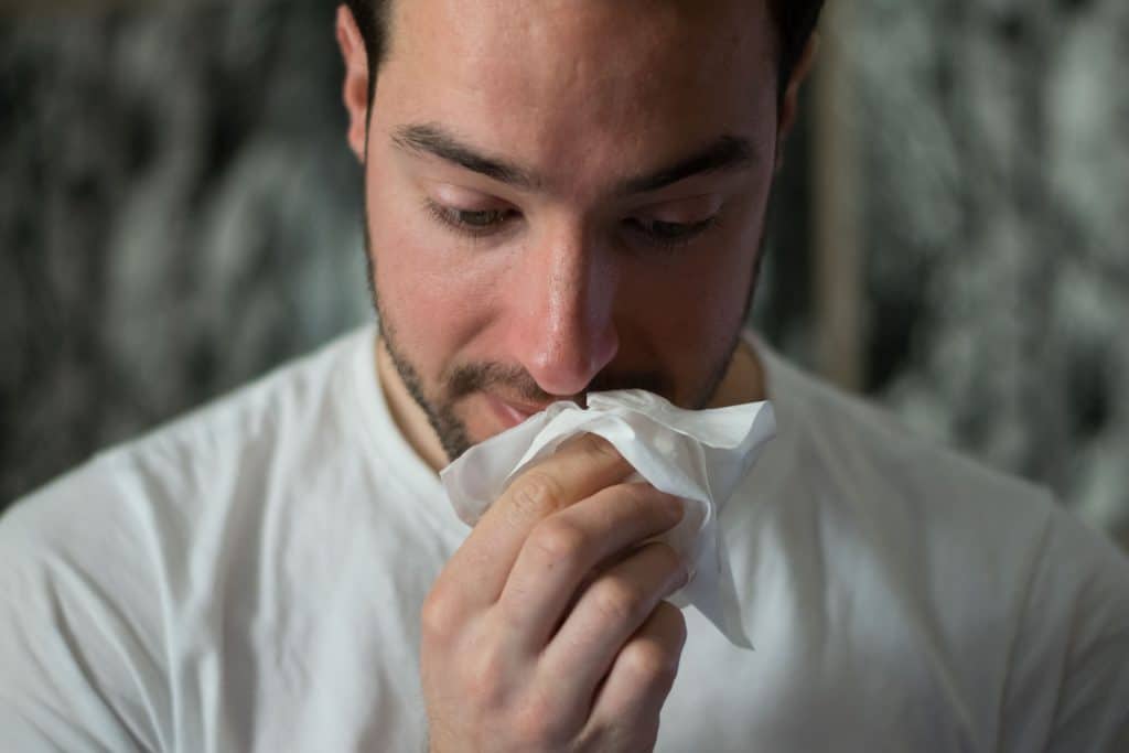 Homem doente limpando o nariz com um lenço de papel.