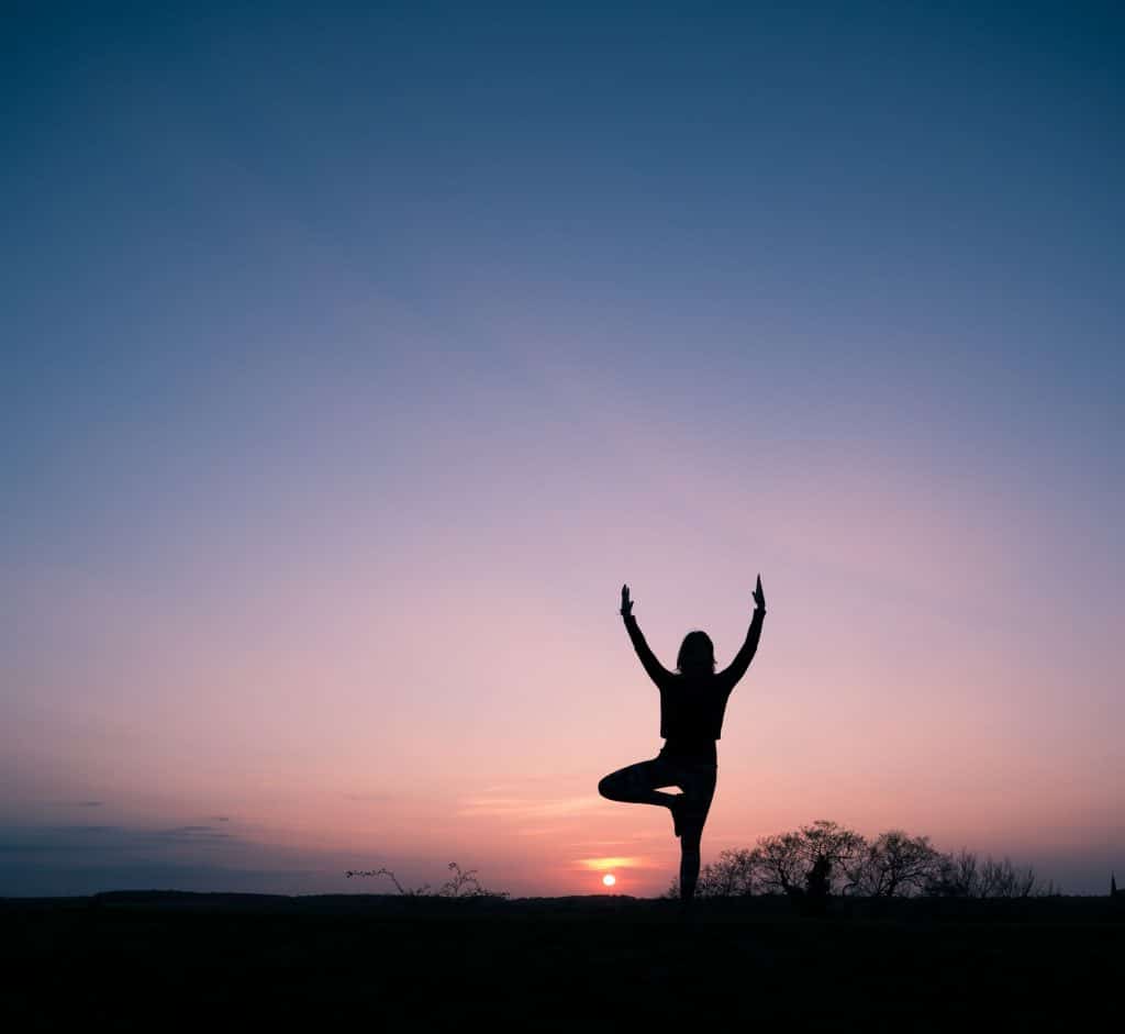 Silhueta de mulher em posição de meditação com sunset ao fundo