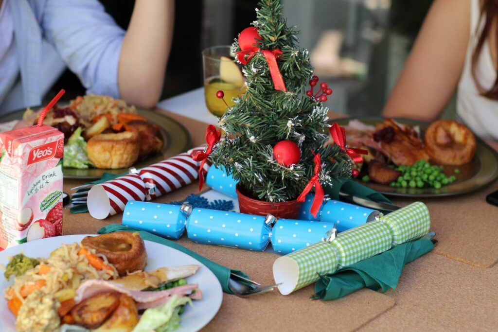 Três pratos de comida cheios em uma mesa com uma árvore de Natal em miniatura no centro.