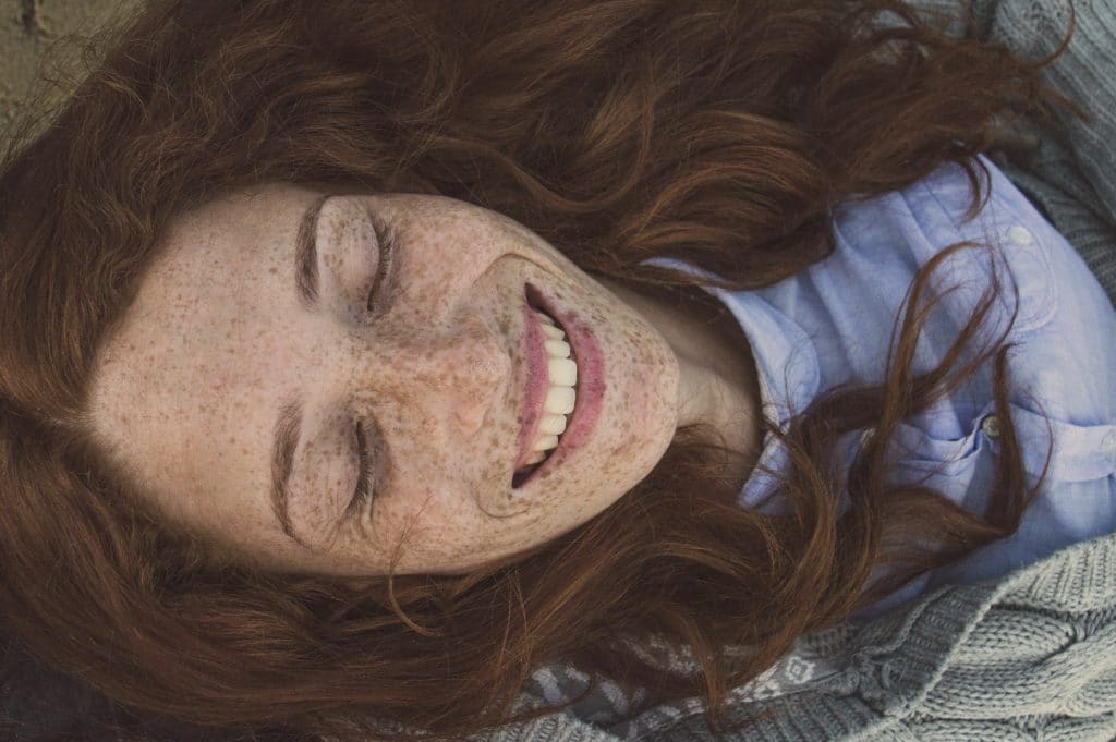 Mulher com sardas no rosto de olhos fechados e cabelo solto