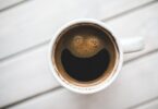 Xícara de café vista de cima, com a espuma do líquido formando um rosto sorridente.