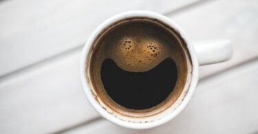 Xícara de café vista de cima, com a espuma do líquido formando um rosto sorridente.