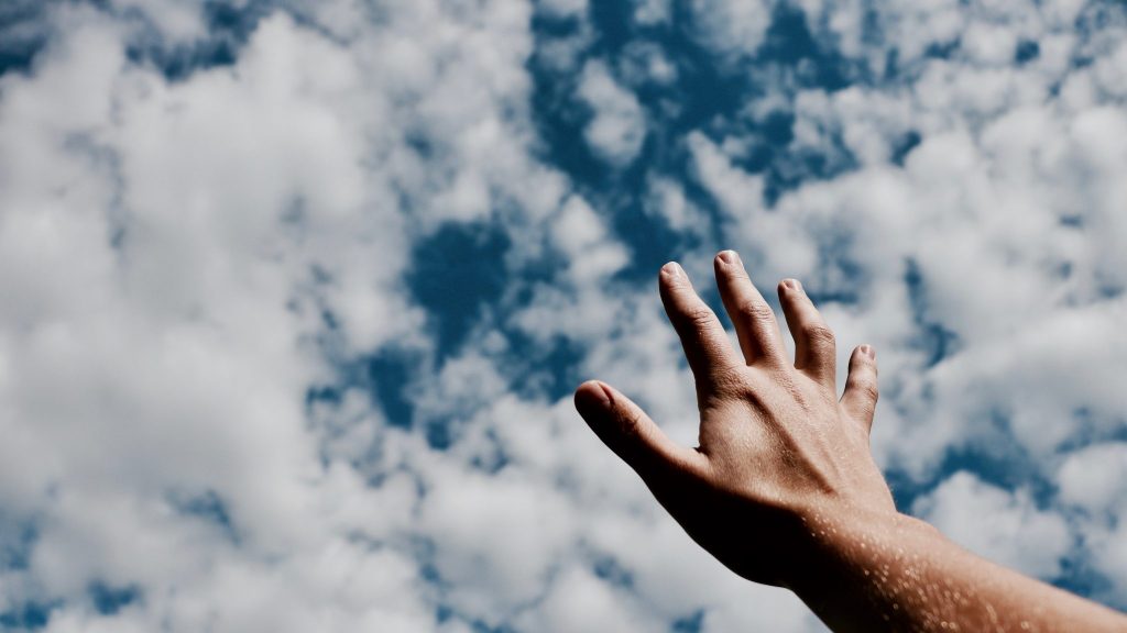 Mão para o céu com nuvens ao fundo