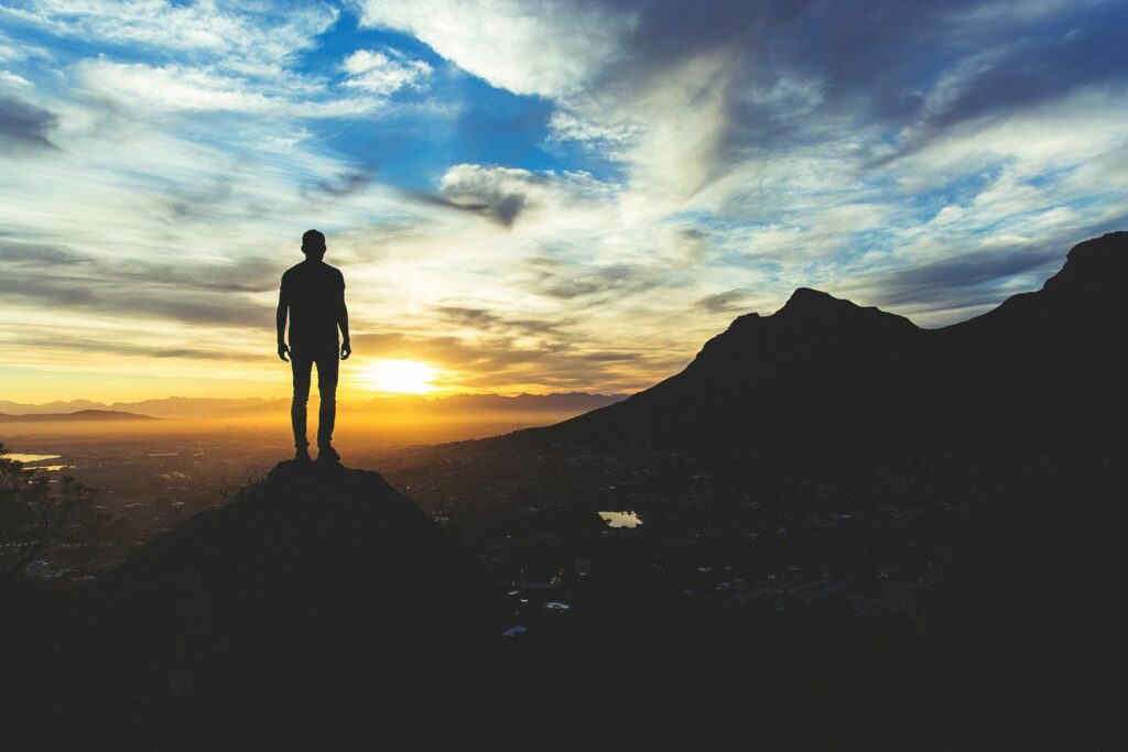 Silhueta de homem em montanha olhando pôr-do-sol