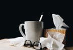 Lenços de papel, óculos e caneca em cima de uma mesa de madeira.