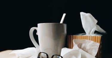 Lenços de papel, óculos e caneca em cima de uma mesa de madeira.