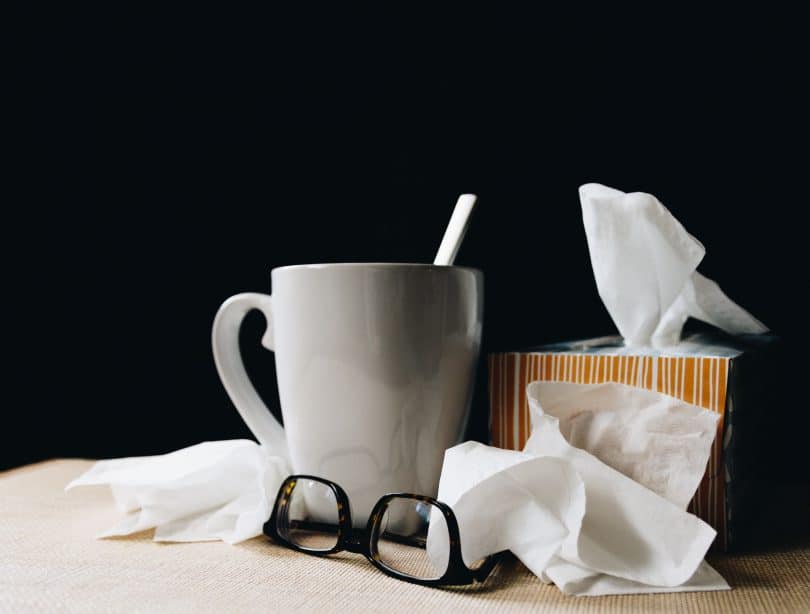 Lenços de papel, óculos e caneca em cima de uma mesa de madeira.