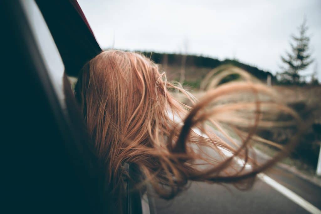 Mulher em janela de carro com cabelos ao vento e estrada ao fundo
