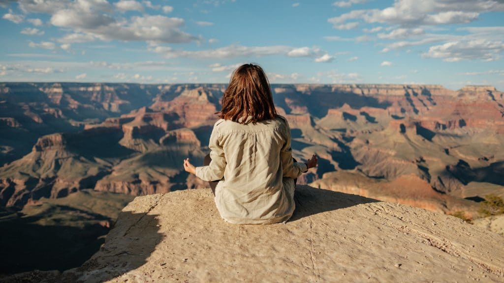 Mulher de costas meditando em montanha com montanhas e céu azul ao fundo