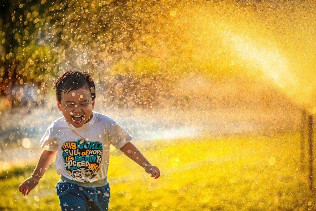 Menino correndo feliz entre esguicho de água