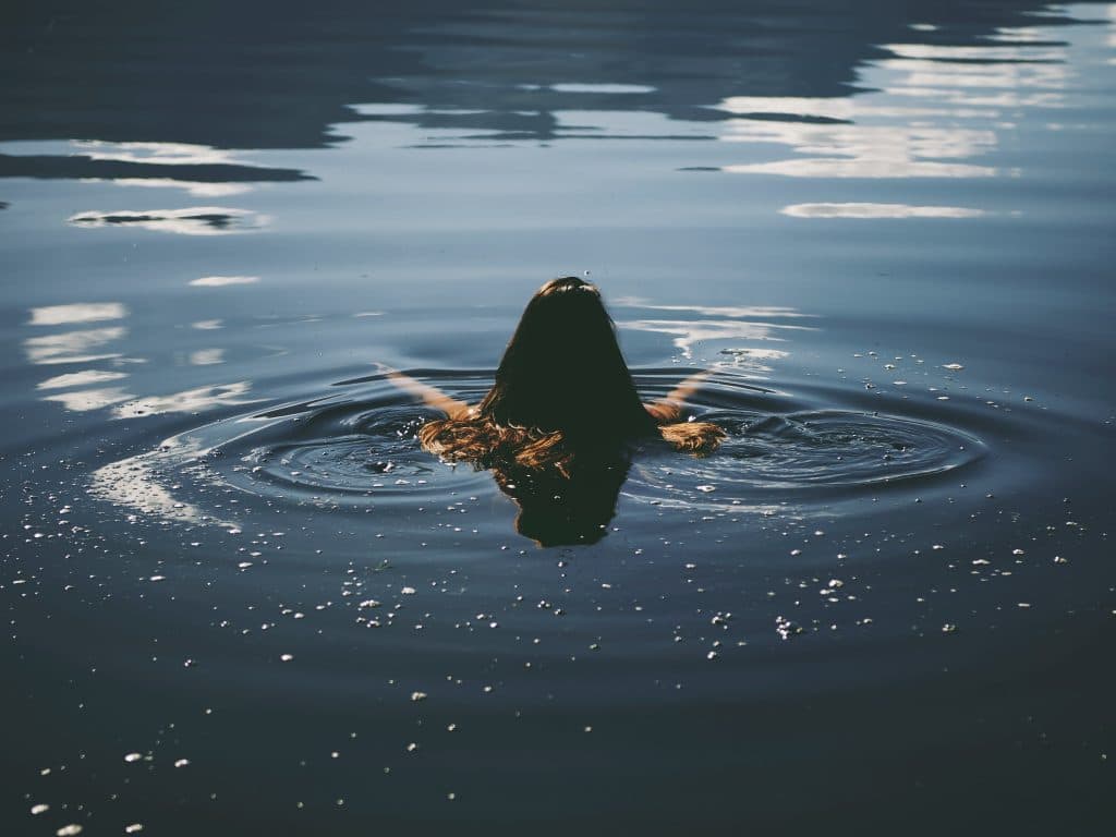 Mulher de costas nadando sozinha em um rio, com os braços abertos.