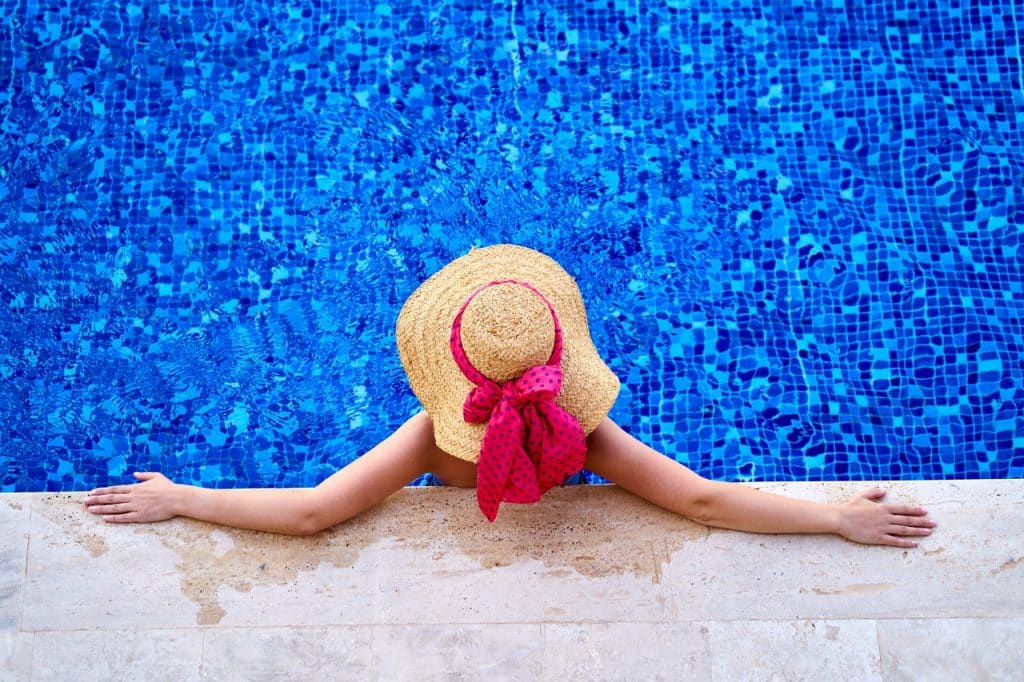 Mulher de costas com chapéu aproveitando a piscina. 