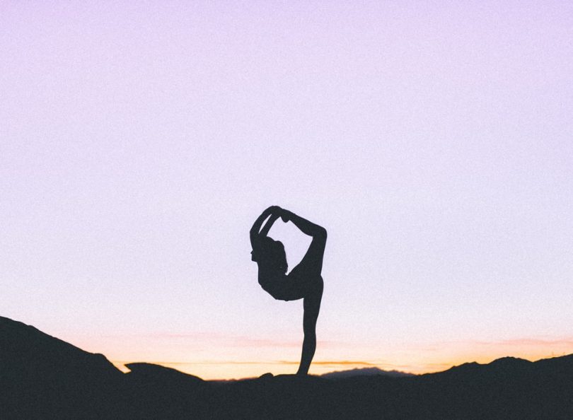 Silhueta de mulher praticando yoga sobre céu arroxeado.