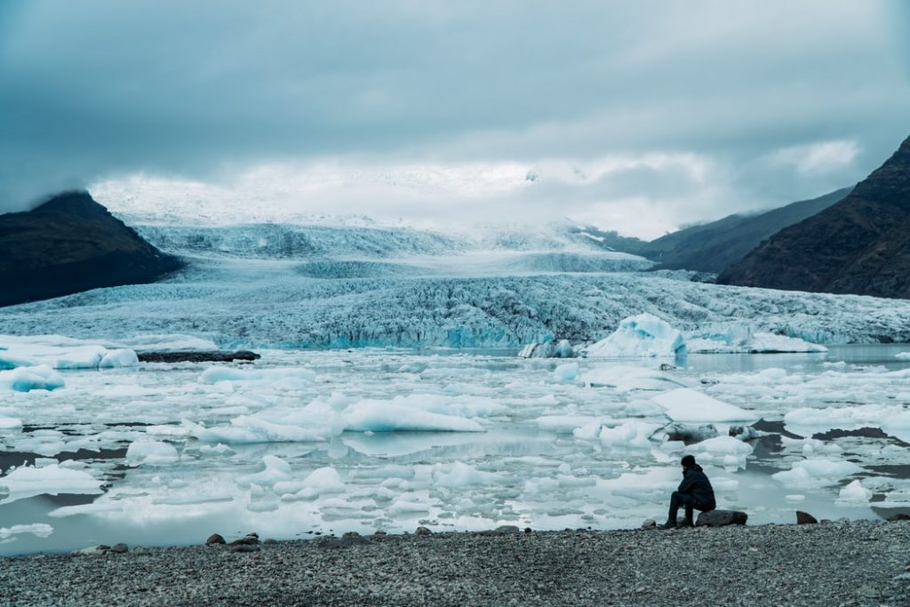 Homem sentado na beira de um lago glacial.