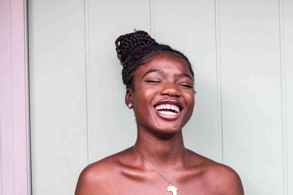 Mulher com cabelo preso sorrindo com olhos fechados