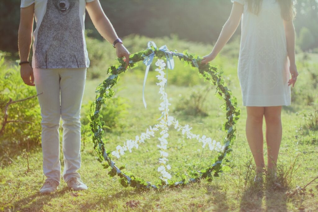 Duas pessoas segurando um aro com o símbolo da paz feito de plantas e flores.