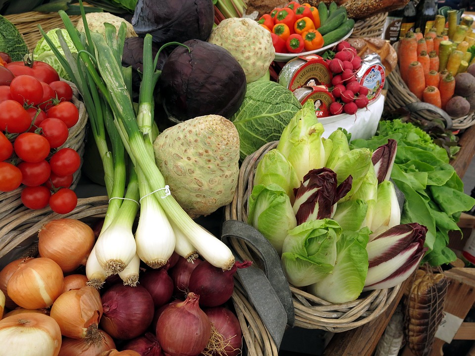 Uma banca com muitos vegetais expostos, como cebolas, cebolas roxas, tomates, alhos-porós, repolhos, cenouras e muitos outros.