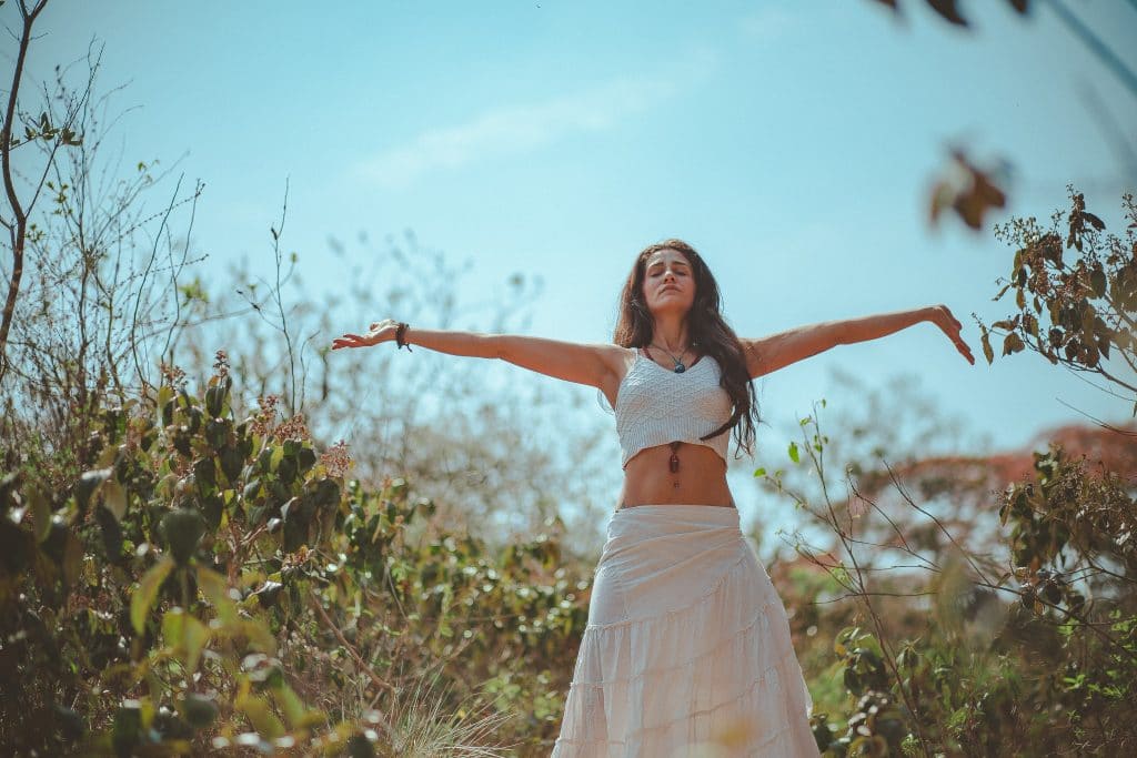 Mulher meditando entre a natureza com braços abertos e olhos fechados