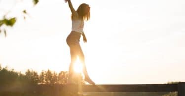 Garota se equilibrando em ponte de madeira com sol refletindo