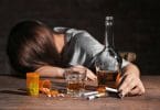 Mulher de cabeça abaixada com mesa com remédios, cigarros e bebida alcoólica