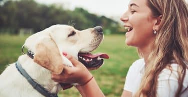 Jovem branca sorrindo segurando rosto de cachorro.