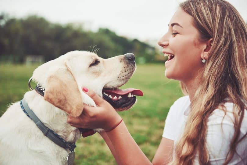 Jovem branca sorrindo segurando rosto de cachorro.