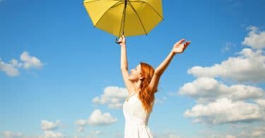 Mulher em campo aberto segurando guarda-chuva amarelo de braços abertos
