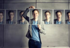 Homem segurando uma foto sorrindo cobrindo seu rosto e atrás diiversas fotos com outras emoções