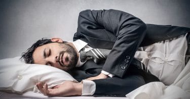 Homem deitado na cama, dormindo, com roupas sociais de trabalho.