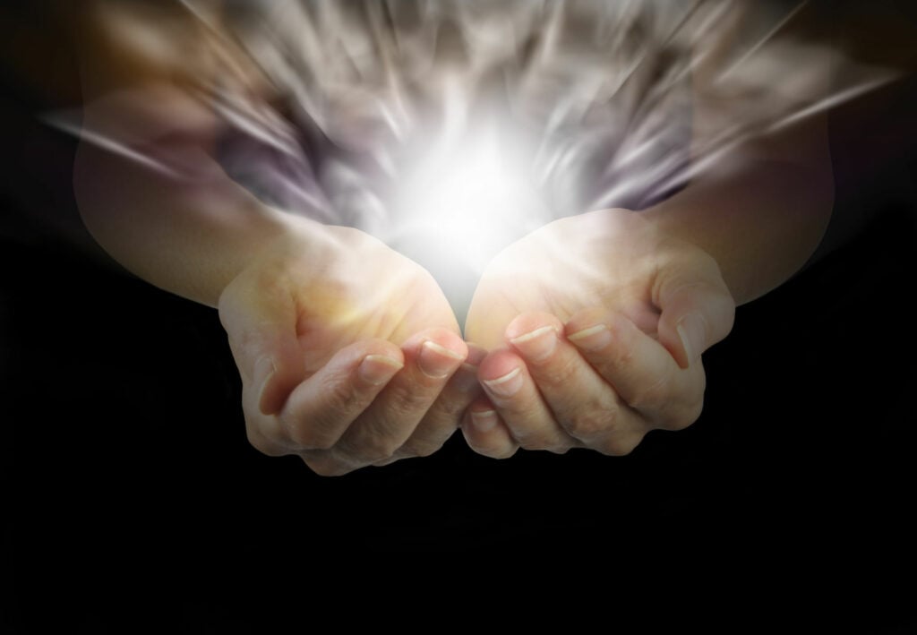 Mãos com as palmas para cima, levemente curvadas, e uma bola de luz sobre elas. A luz representa energia do Reiki.