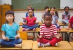 Alunos meditando em posição de lótus na mesa na sala de aula na escola primária
