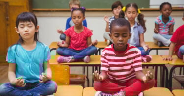Alunos meditando em posição de lótus na mesa na sala de aula na escola primária