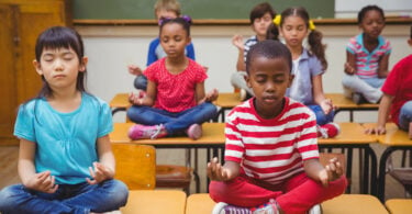 Alunos meditando em posição de lótus na mesa na sala de aula na escola primária