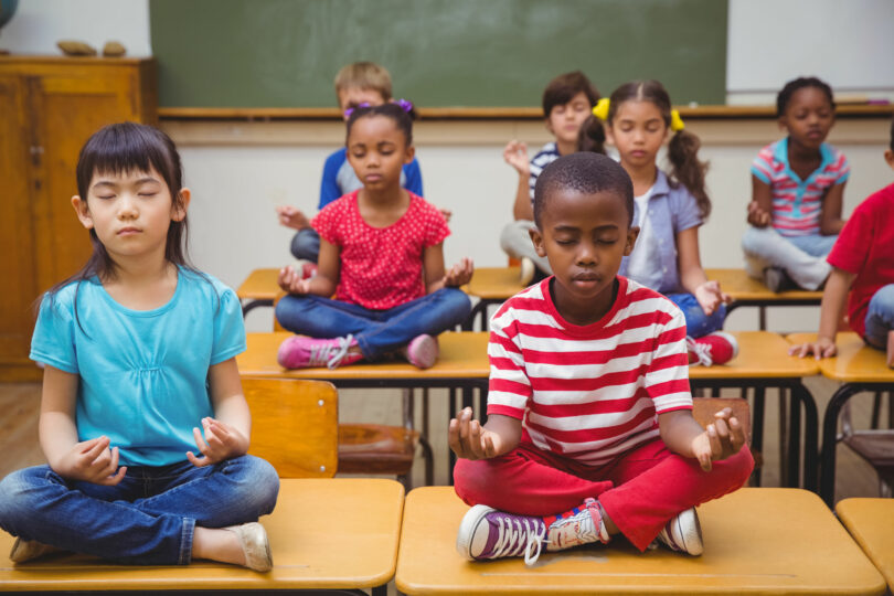 Alunos meditando em posição de lótus na mesa na sala de aula na escola primária