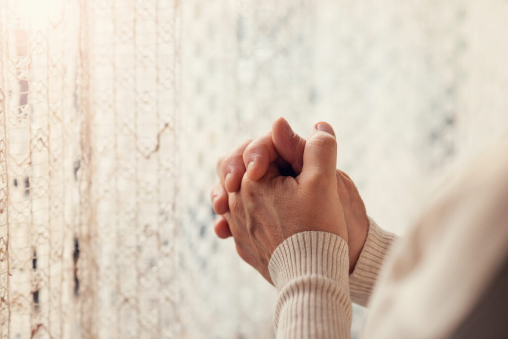 Mulher com as mãos juntas rezando ao lado da janela