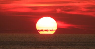 Sol grande por estar muito próximo da Terra, se pondo no horizonte do mar.