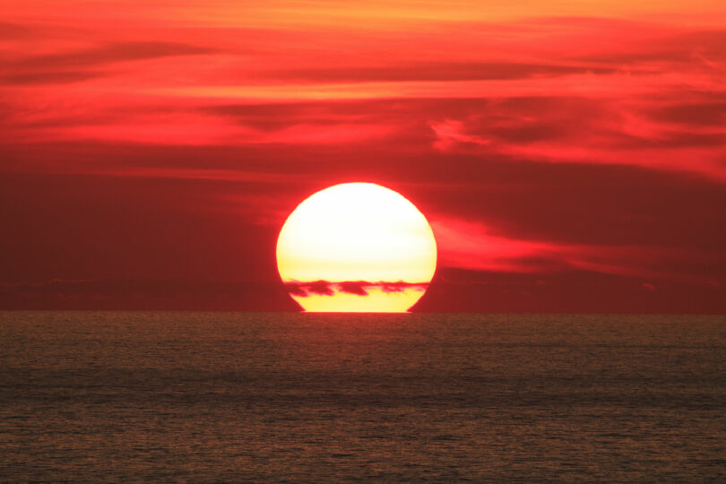 Sol grande por estar muito próximo da Terra, se pondo no horizonte do mar.