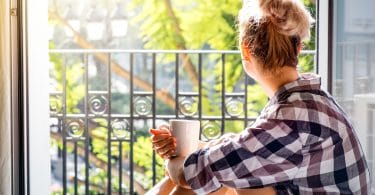 Mulher olhando para varanda enquanto segura uma xícara de café