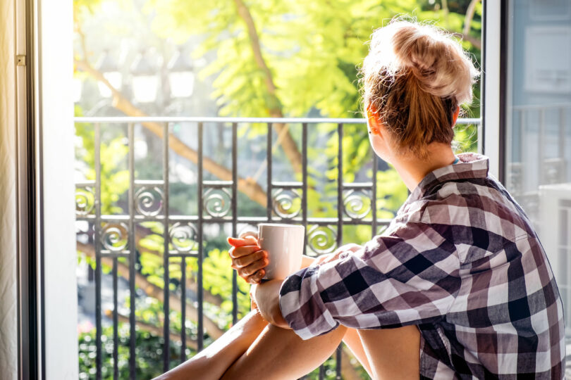 Mulher olhando para varanda enquanto segura uma xícara de café